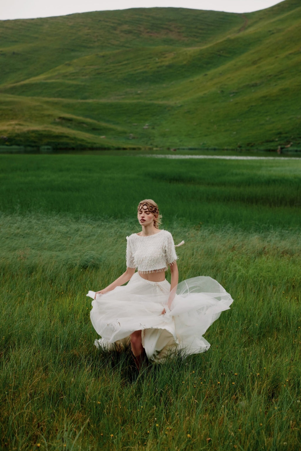 Woman in a white dress standing in a green field with rolling hills in the background