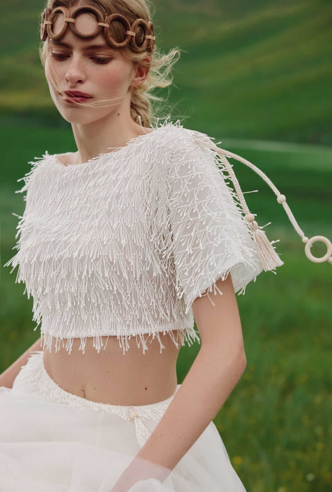 Woman wearing a white fringe top and skirt with a green field background