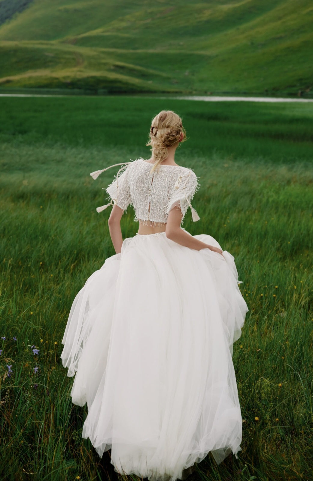 Woman in a white dress standing in a green field with rolling hills in the background