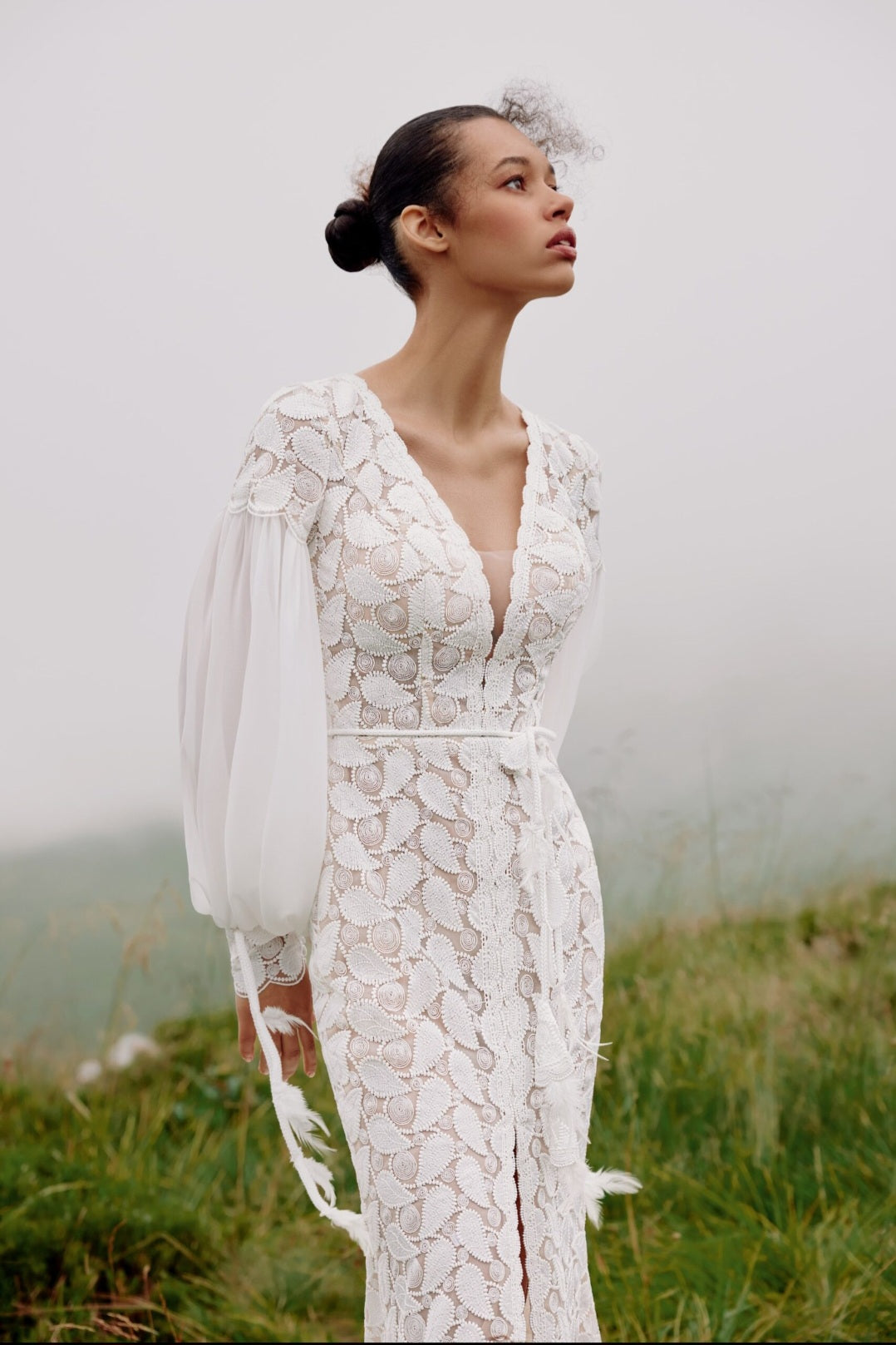 Woman in a white lace dress standing in a grassy field with a blurred background