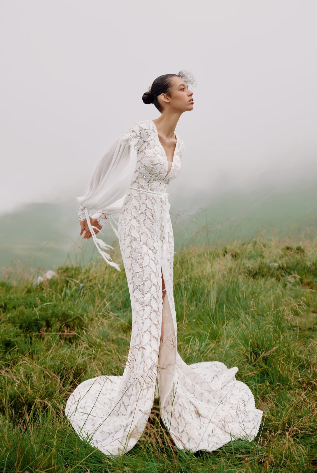 Woman in a white wedding dress standing on a grassy hill with a misty background