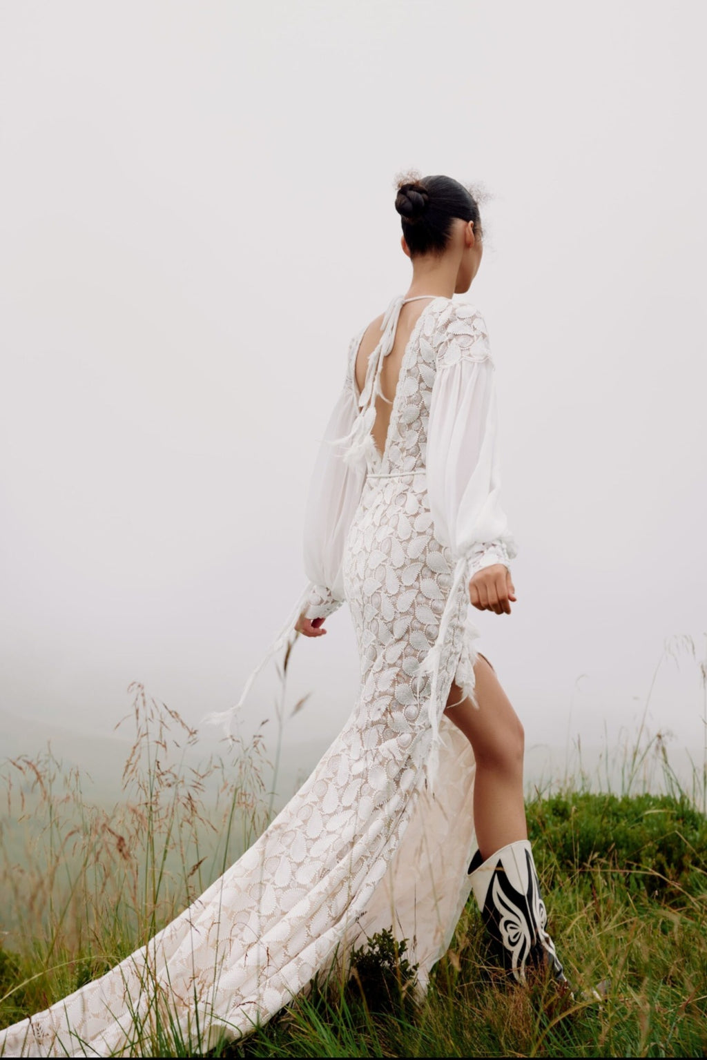 Woman in a white lace dress standing in a grassy field with a foggy background