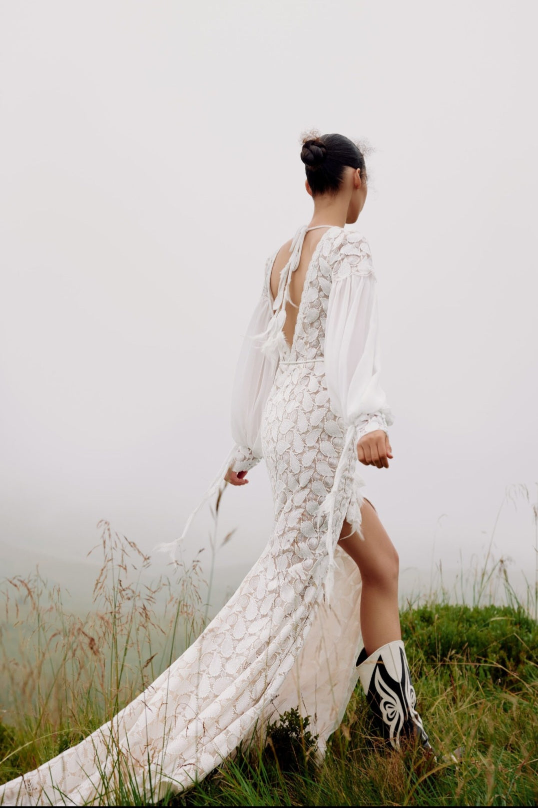 Woman in a white lace dress standing in a grassy field with a foggy background