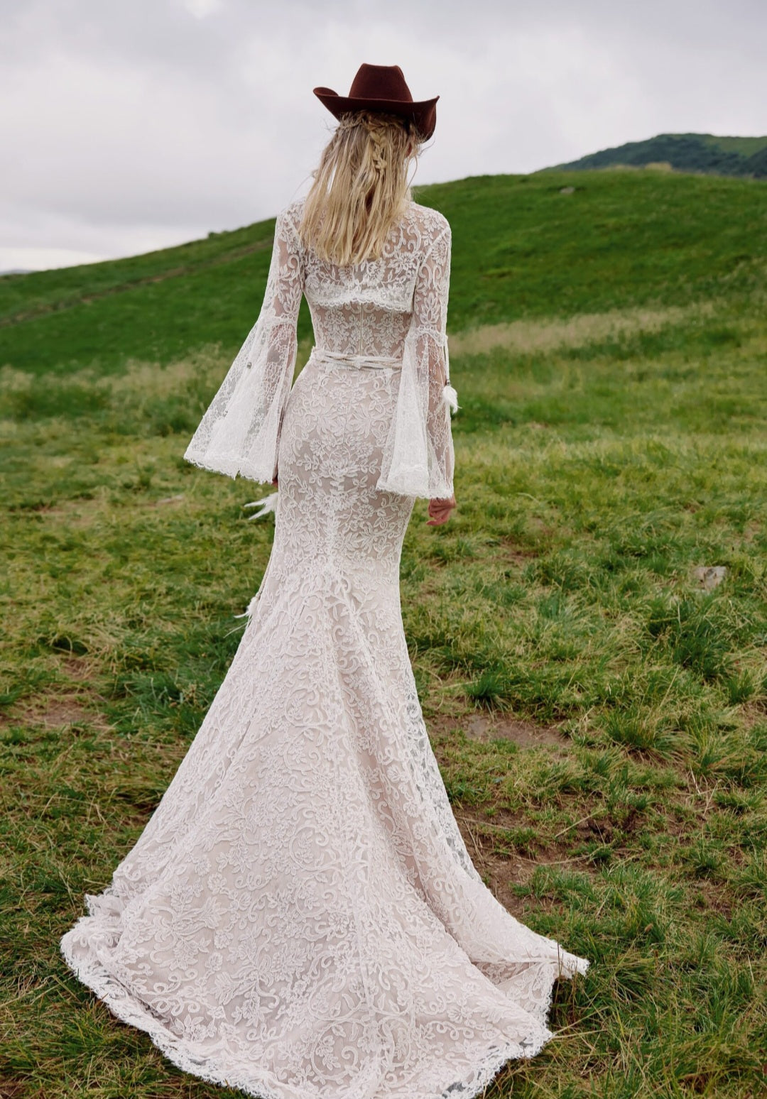 Woman in a lace dress and cowboy hat standing in a grassy field