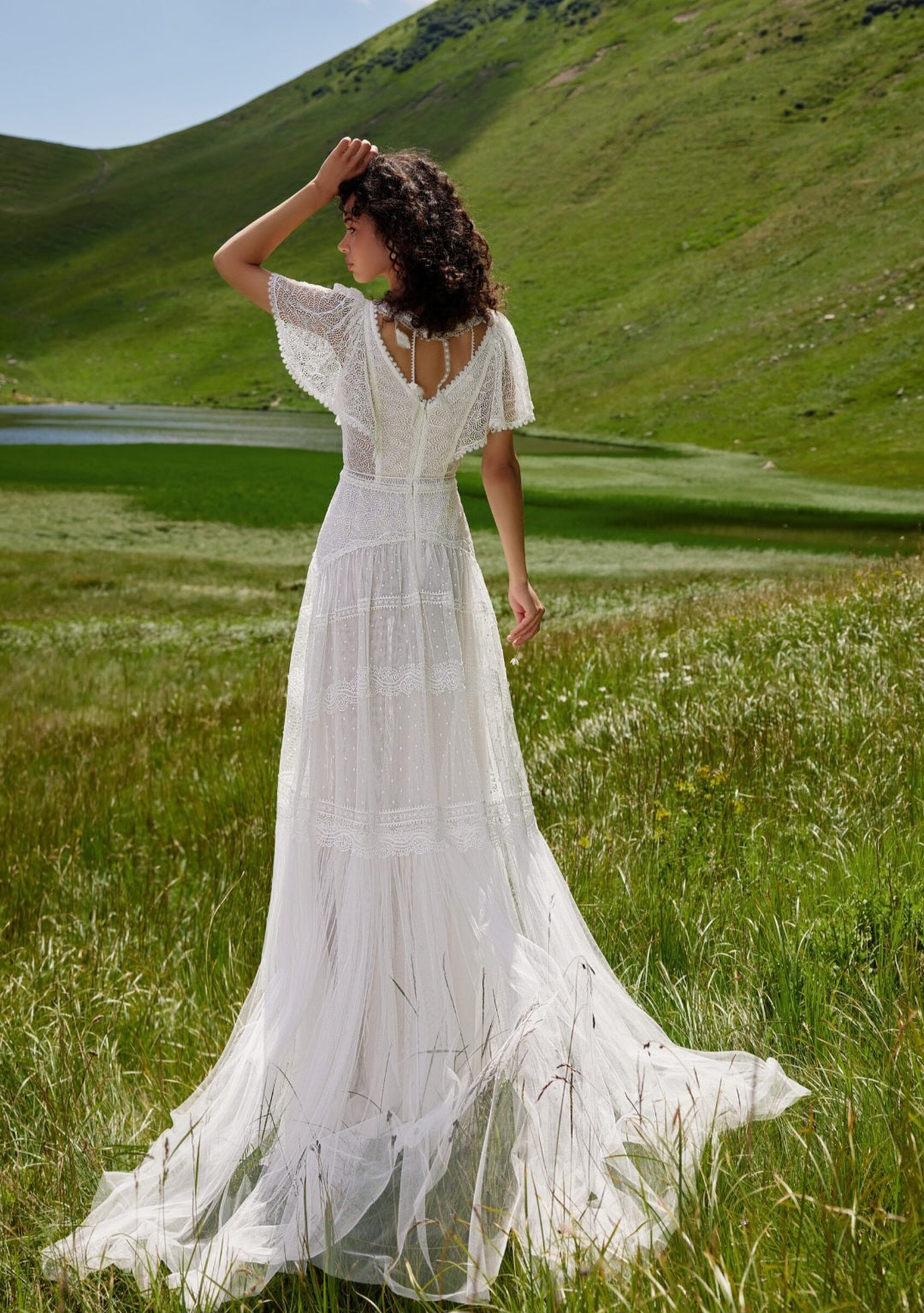 Woman in a white dress standing in a grassy field with mountains in the background