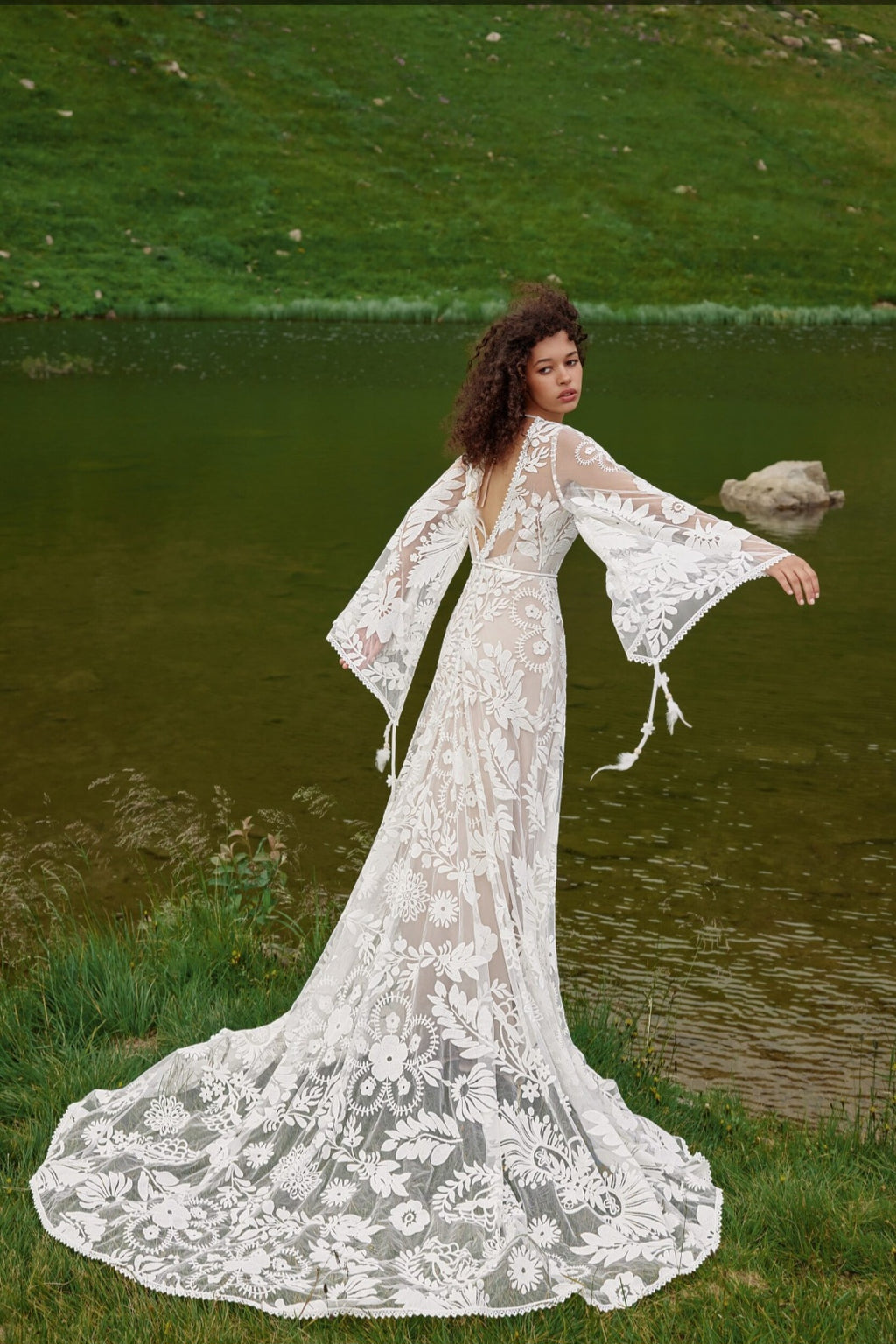Woman in a lace dress standing by a body of water with greenery in the background