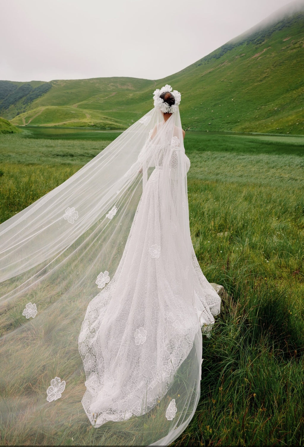 Person in a white wedding dress with a long veil standing in a green field.