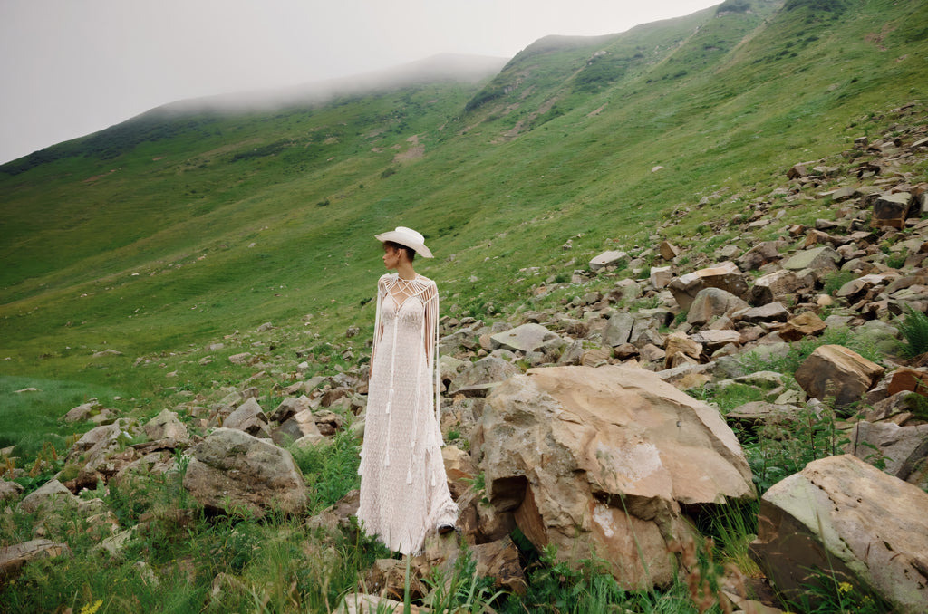 Person in a white dress standing on a rocky hillside with green valleys in the background