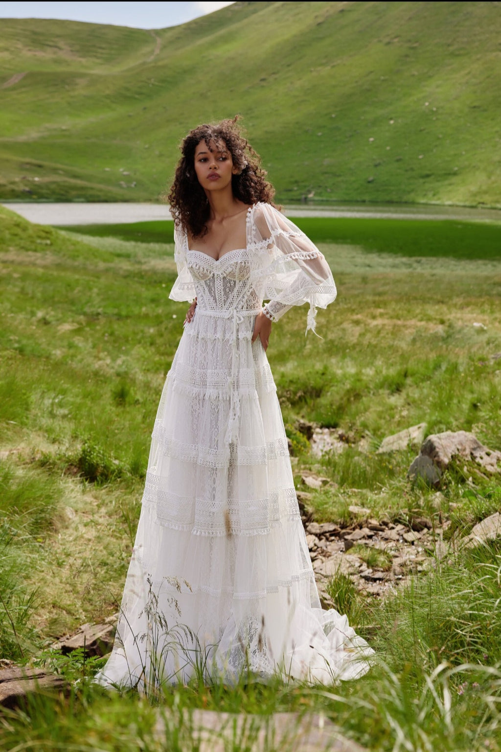 Woman in a white dress standing in a grassy field with a lake in the background
