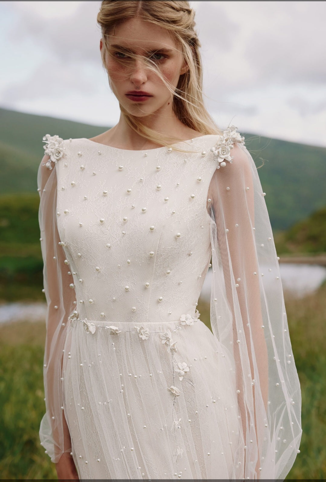 Woman wearing a white wedding dress with floral embellishments in a natural setting.