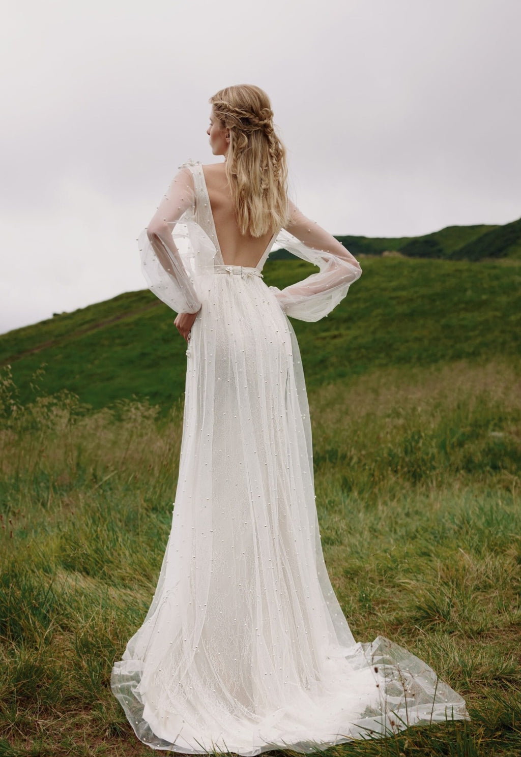 Woman in a white wedding dress standing in a grassy field with a scenic background