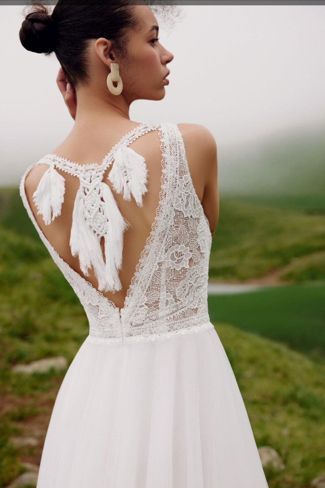 Woman wearing a white lace wedding dress with feather details in a natural setting.
