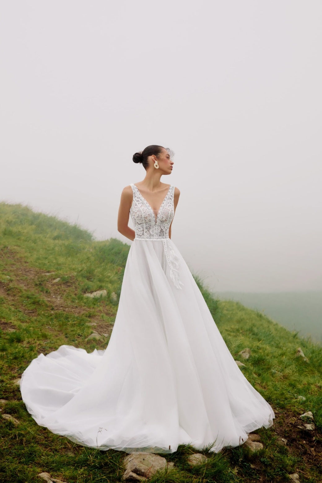 Woman in a white wedding dress standing on a grassy hill with a foggy background