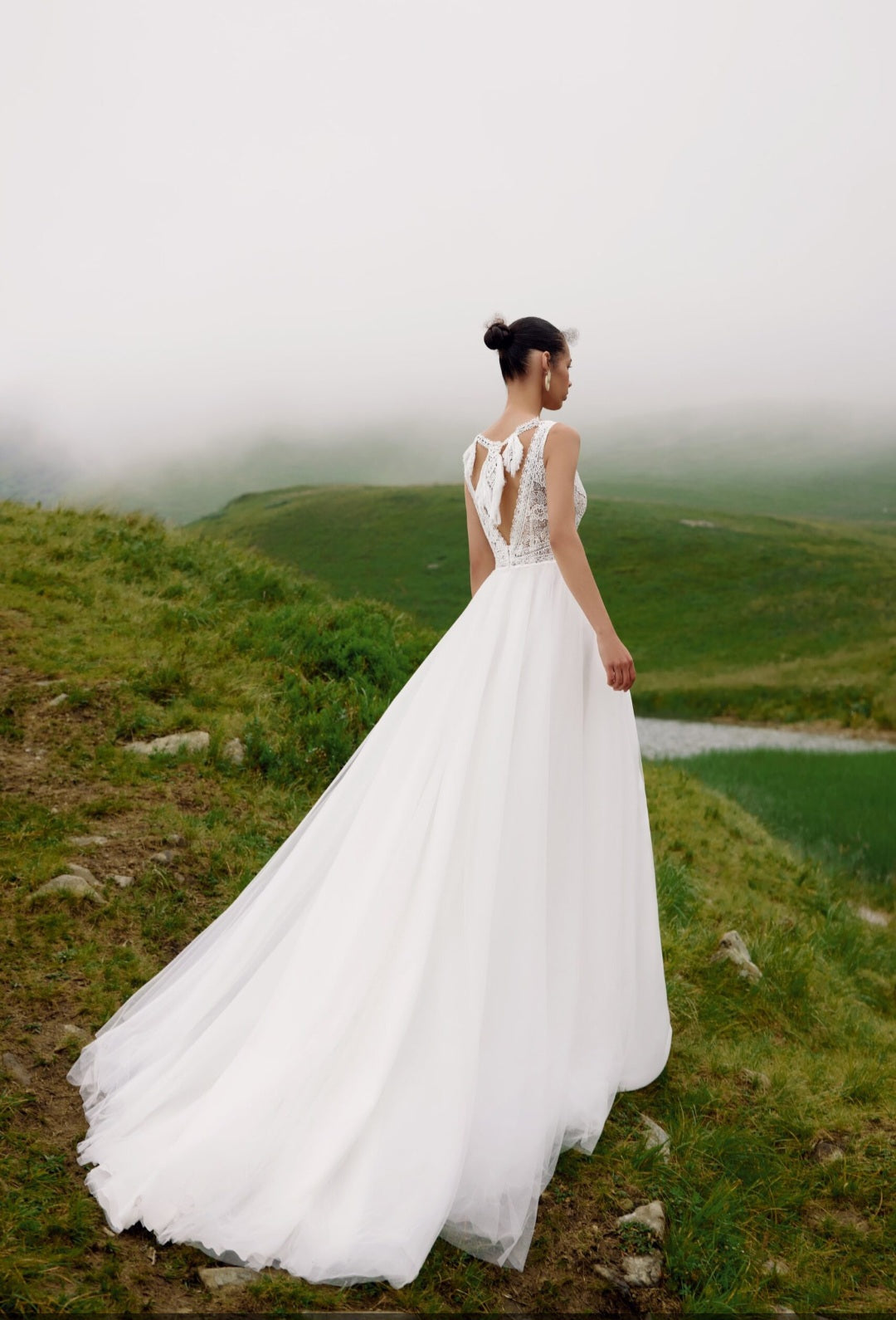 Woman in a white wedding dress standing on a grassy hill with a foggy background
