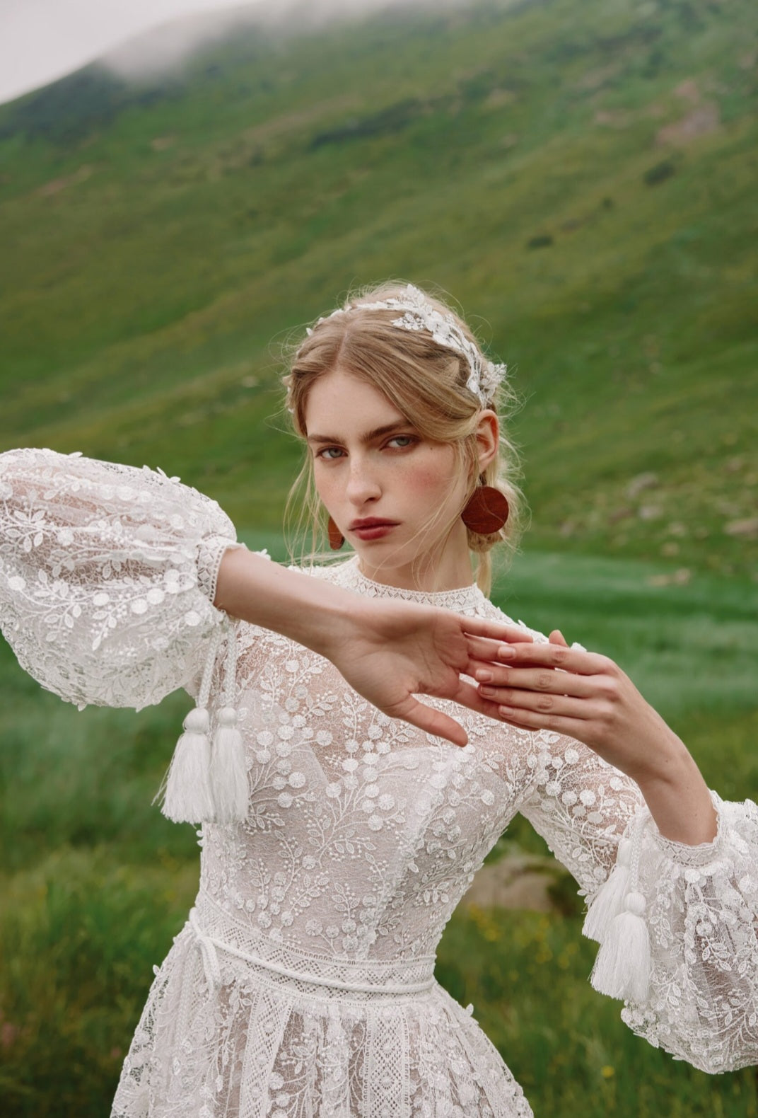 Woman in a white lace dress with puffed sleeves standing in a green field.