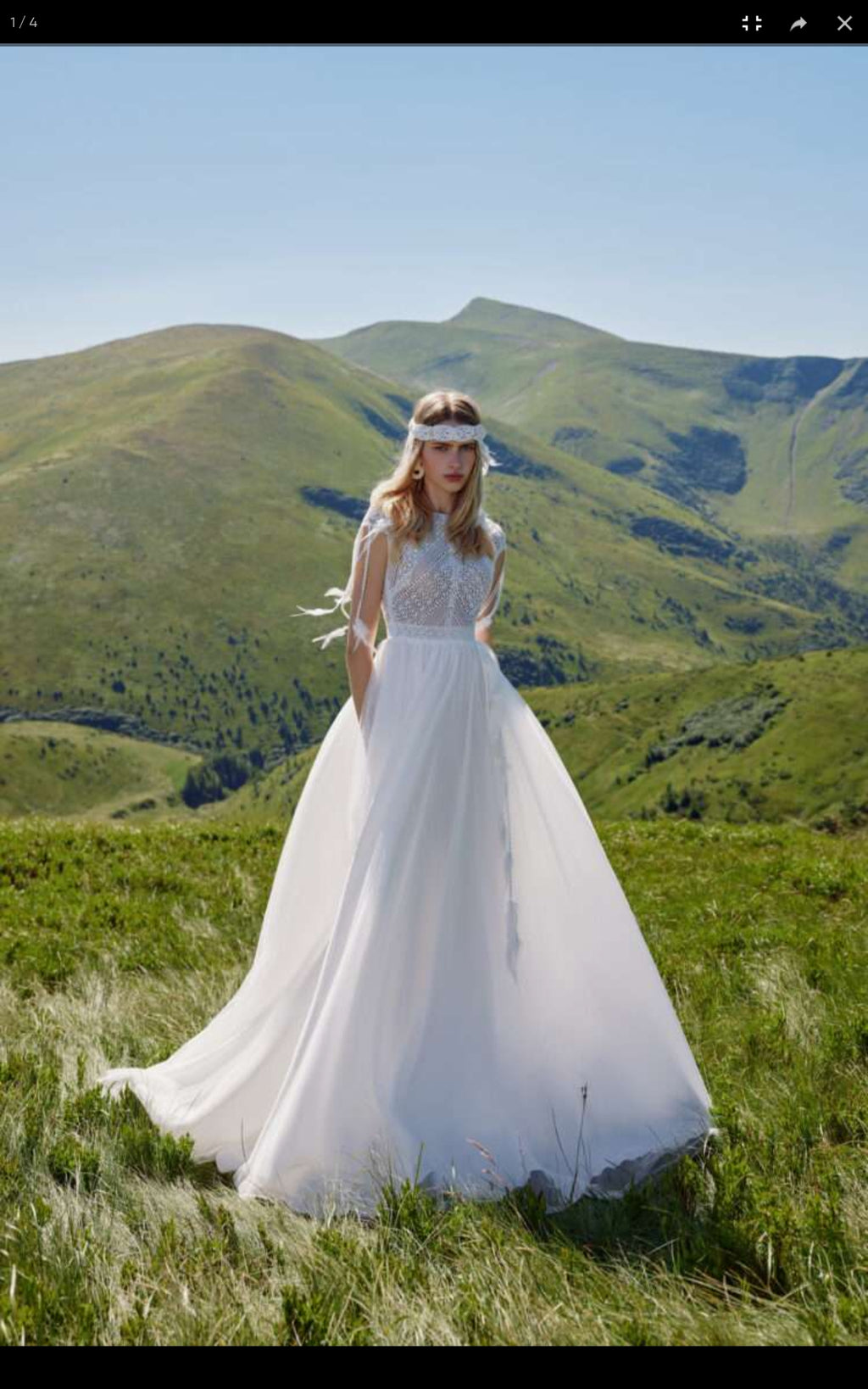 Woman in a white wedding dress standing in a grassy field with mountains in the background