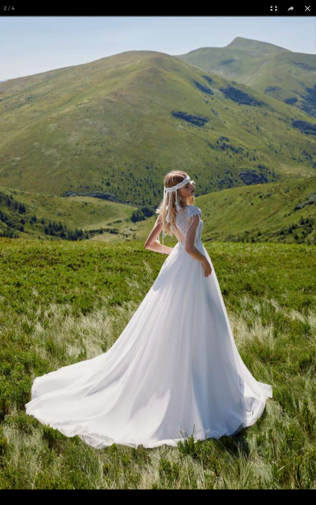 Woman in a white wedding dress standing in a grassy field with mountains in the background