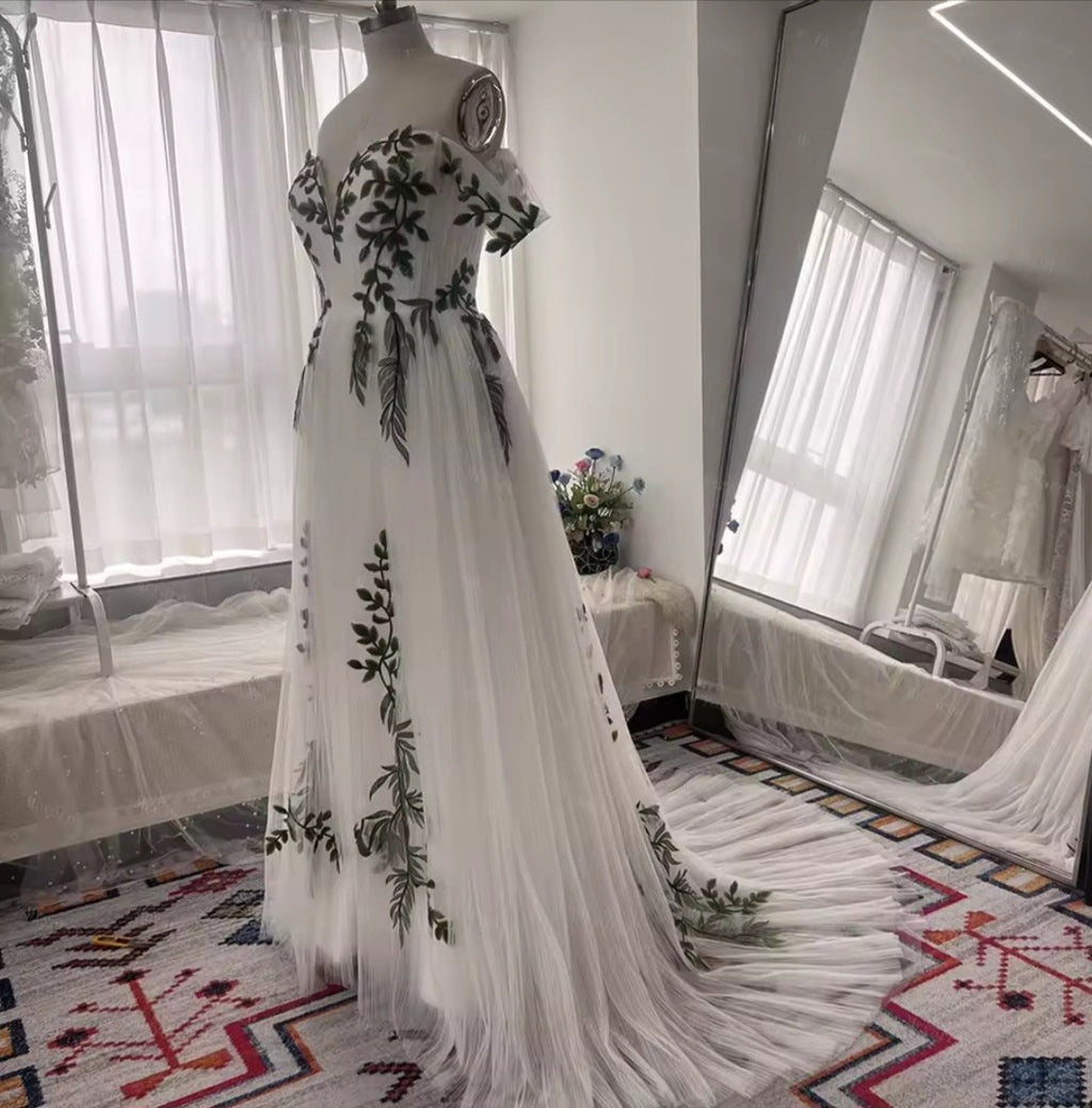 White evening gown with green floral embroidery on a mannequin in a room.