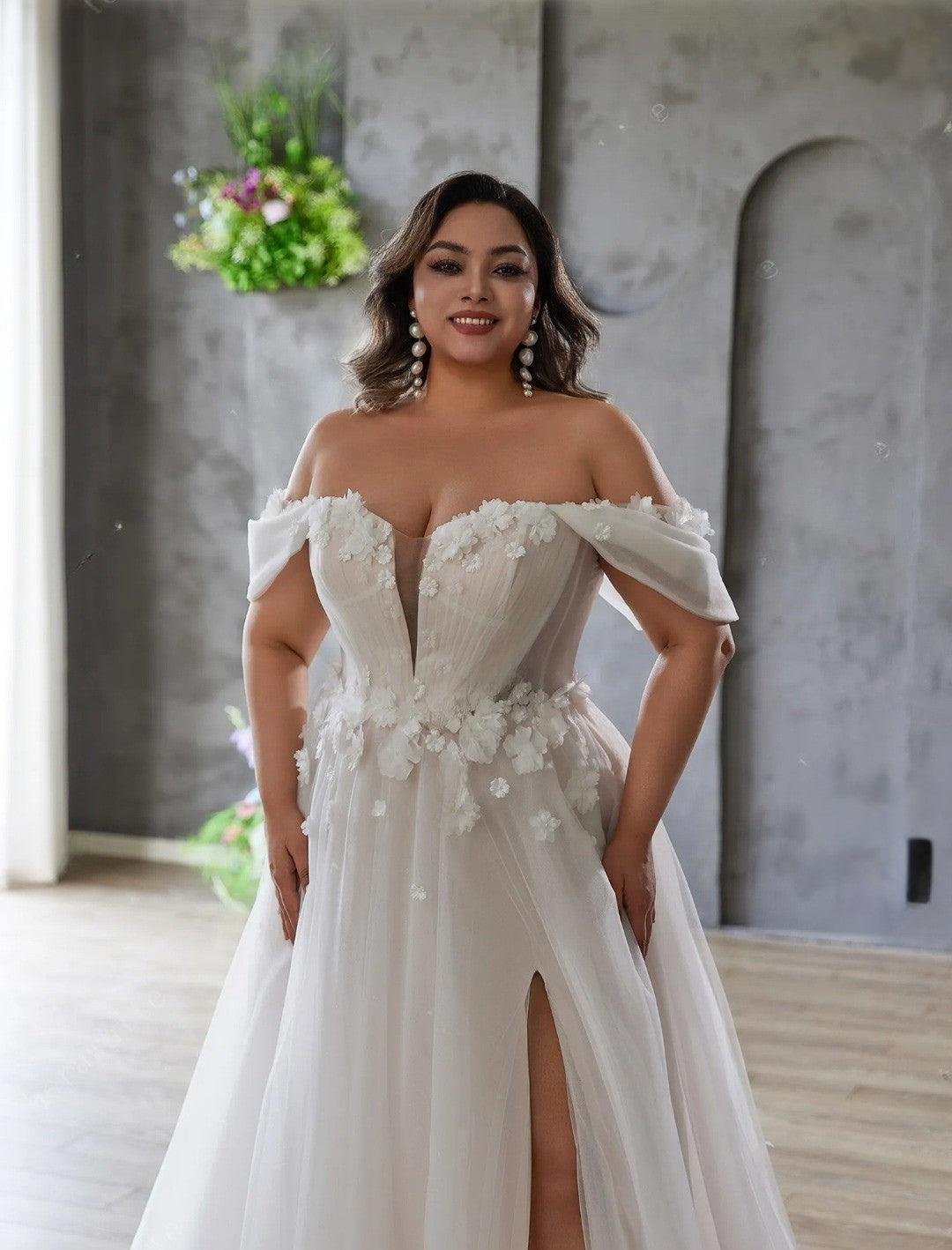 Woman wearing a white off-shoulder gown with floral details in an indoor setting.