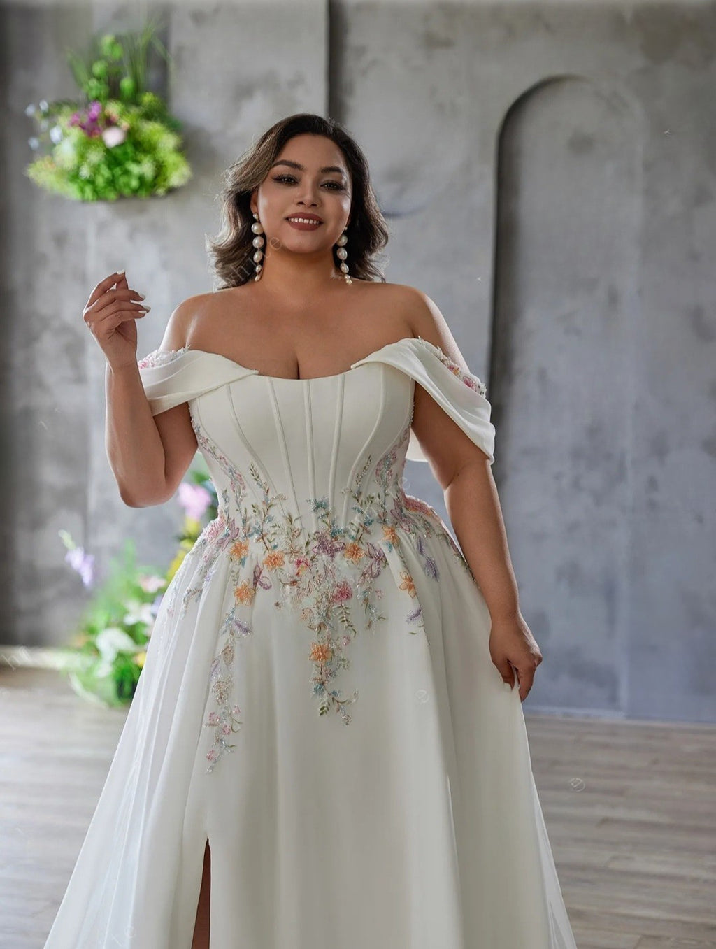 Woman wearing a white off-shoulder dress with floral embroidery in a room with decorative plants.