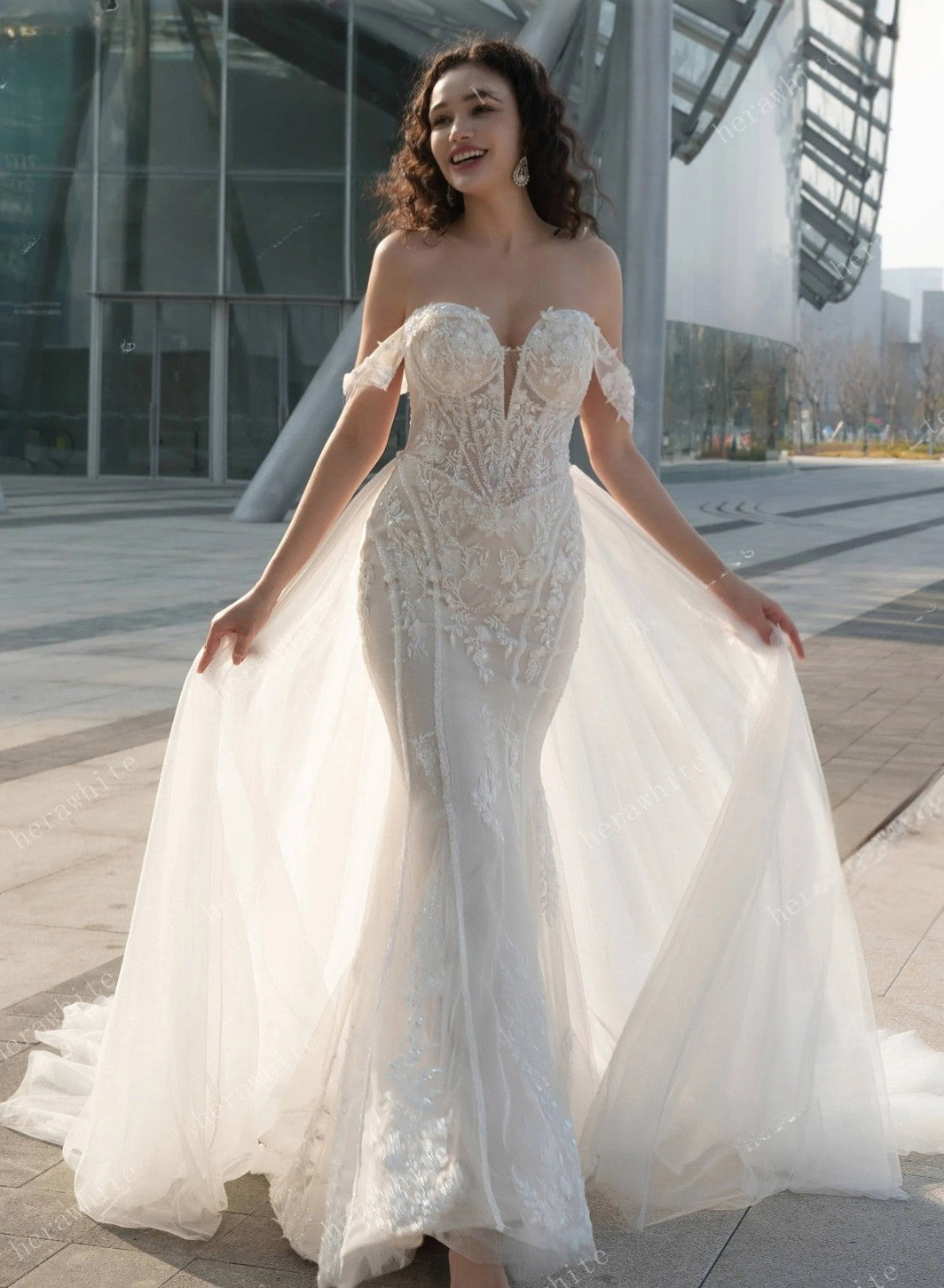 Woman in a white wedding dress standing outdoors with modern architecture in the background