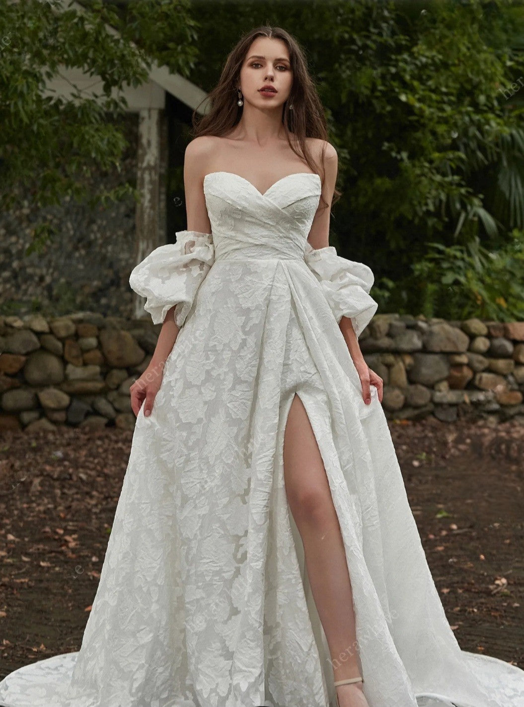 Woman wearing a white lace wedding dress with ruffled sleeves in a natural setting.