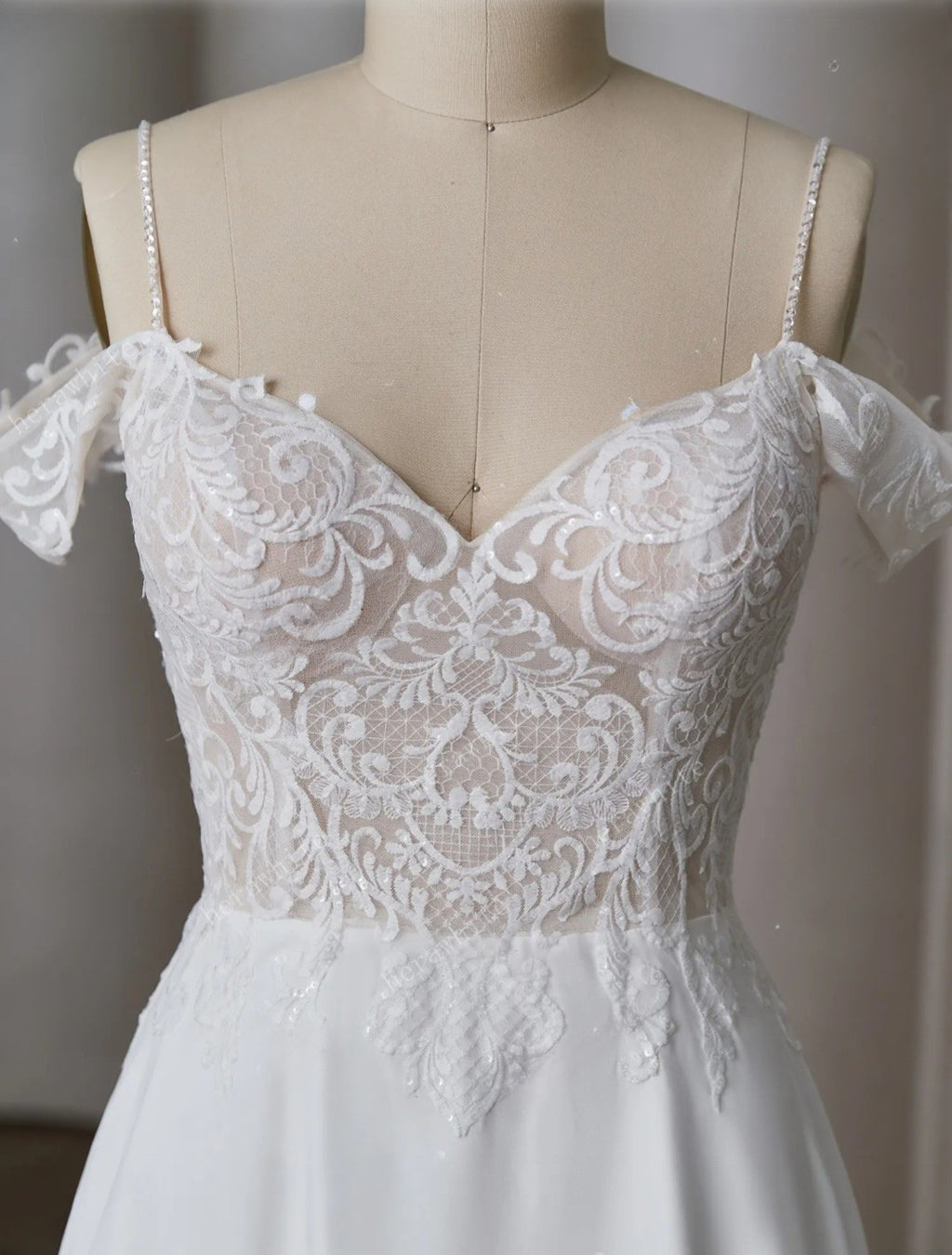 White lace wedding dress on a mannequin against a neutral background