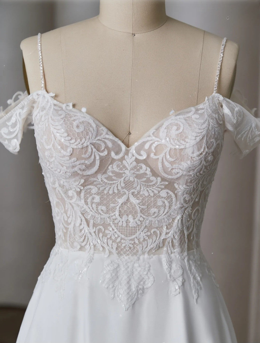 White lace wedding dress on a mannequin against a neutral background