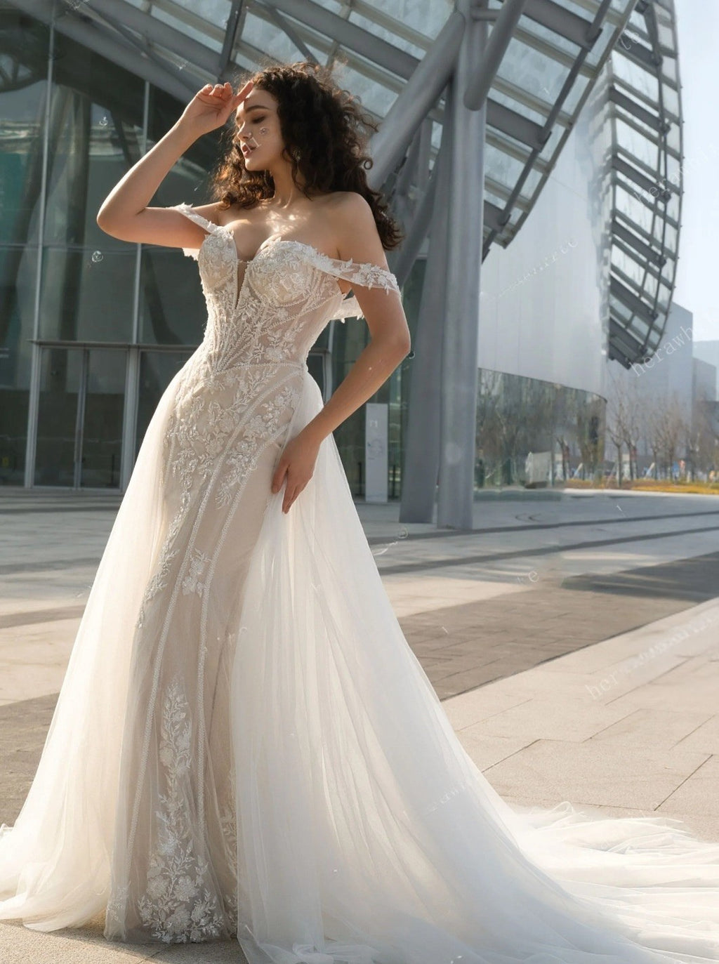Woman in a white lace wedding dress standing in an urban setting.