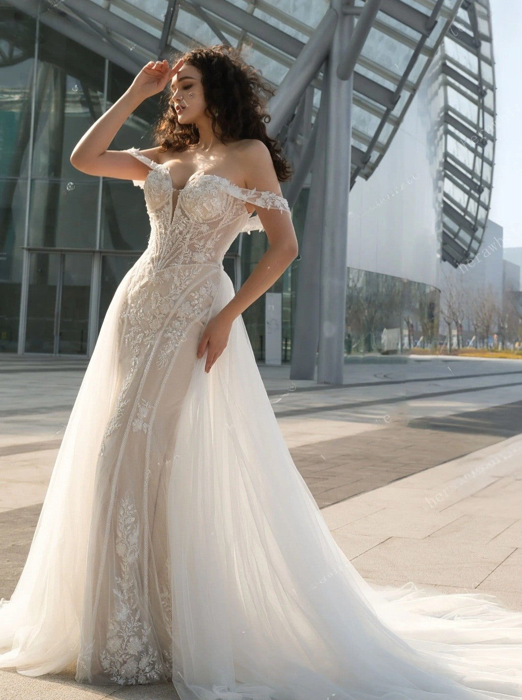 Woman in a white lace wedding dress standing in an urban setting.