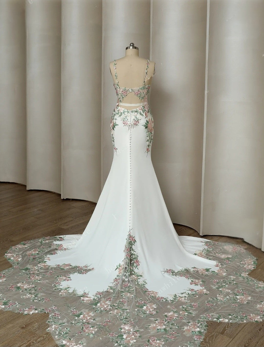 White wedding dress with floral details on a mannequin against a neutral curtain background