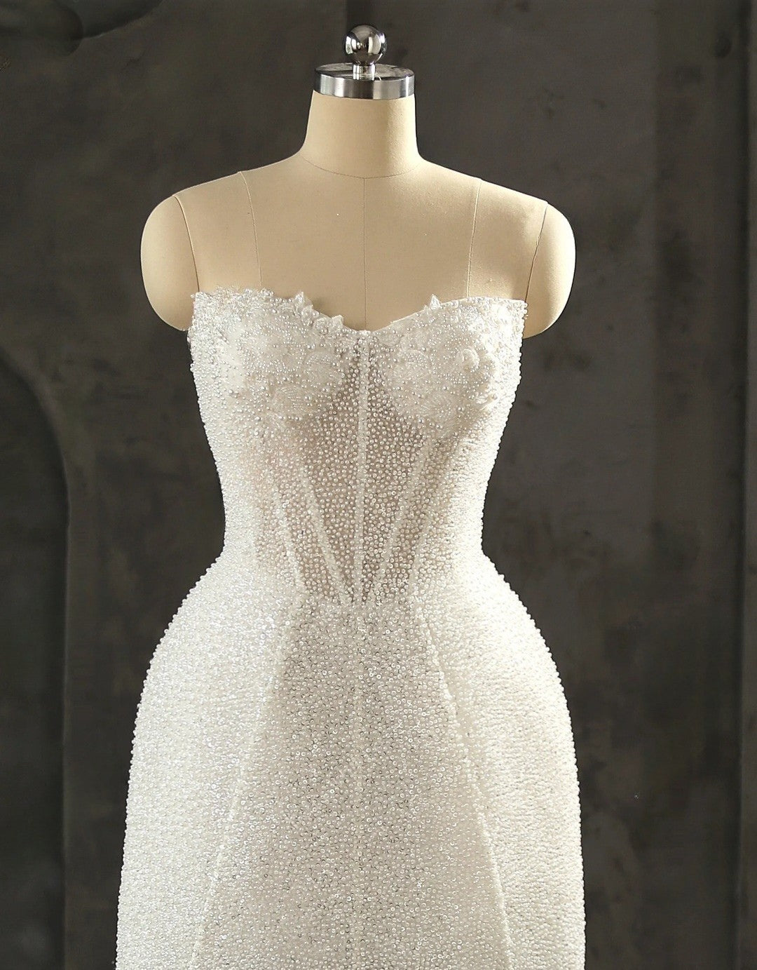 White beaded dress on a mannequin against a dark background