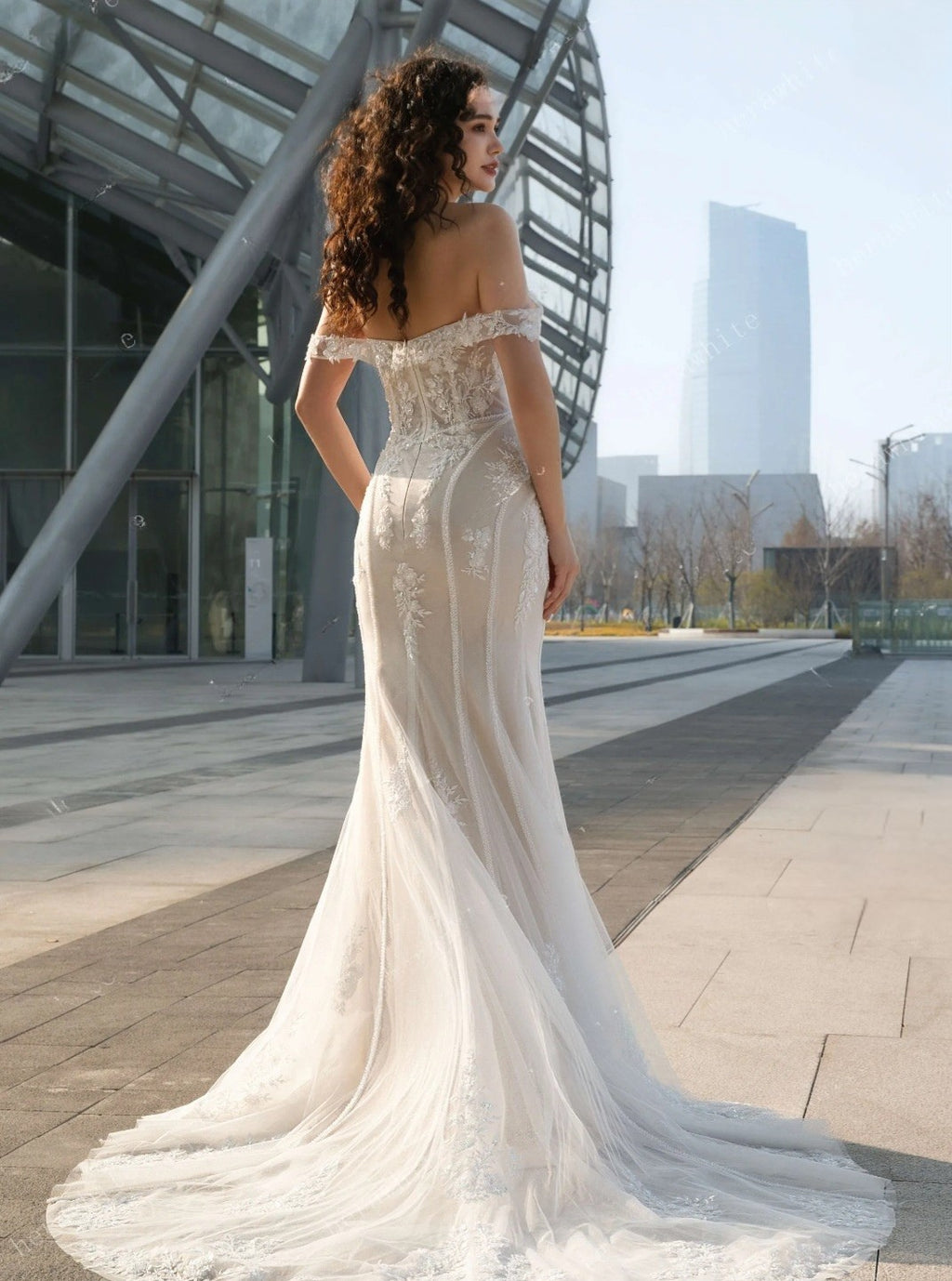 Woman in a white off-shoulder wedding dress standing in an urban setting.