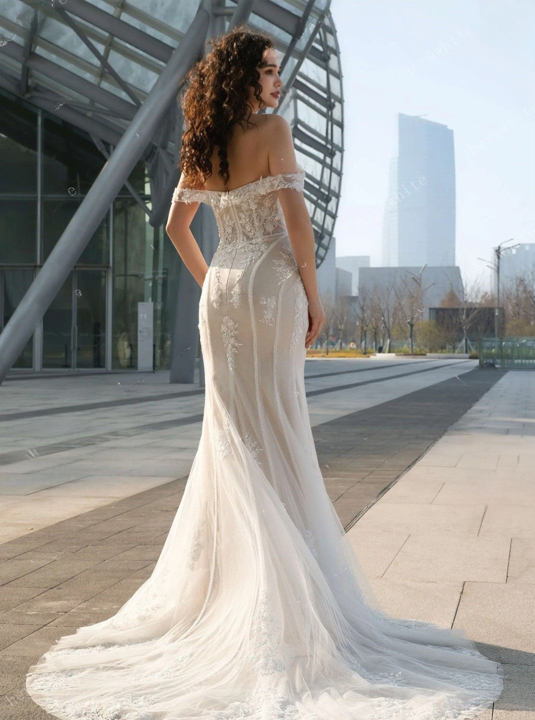 Woman in a white off-shoulder wedding dress standing in an urban setting.