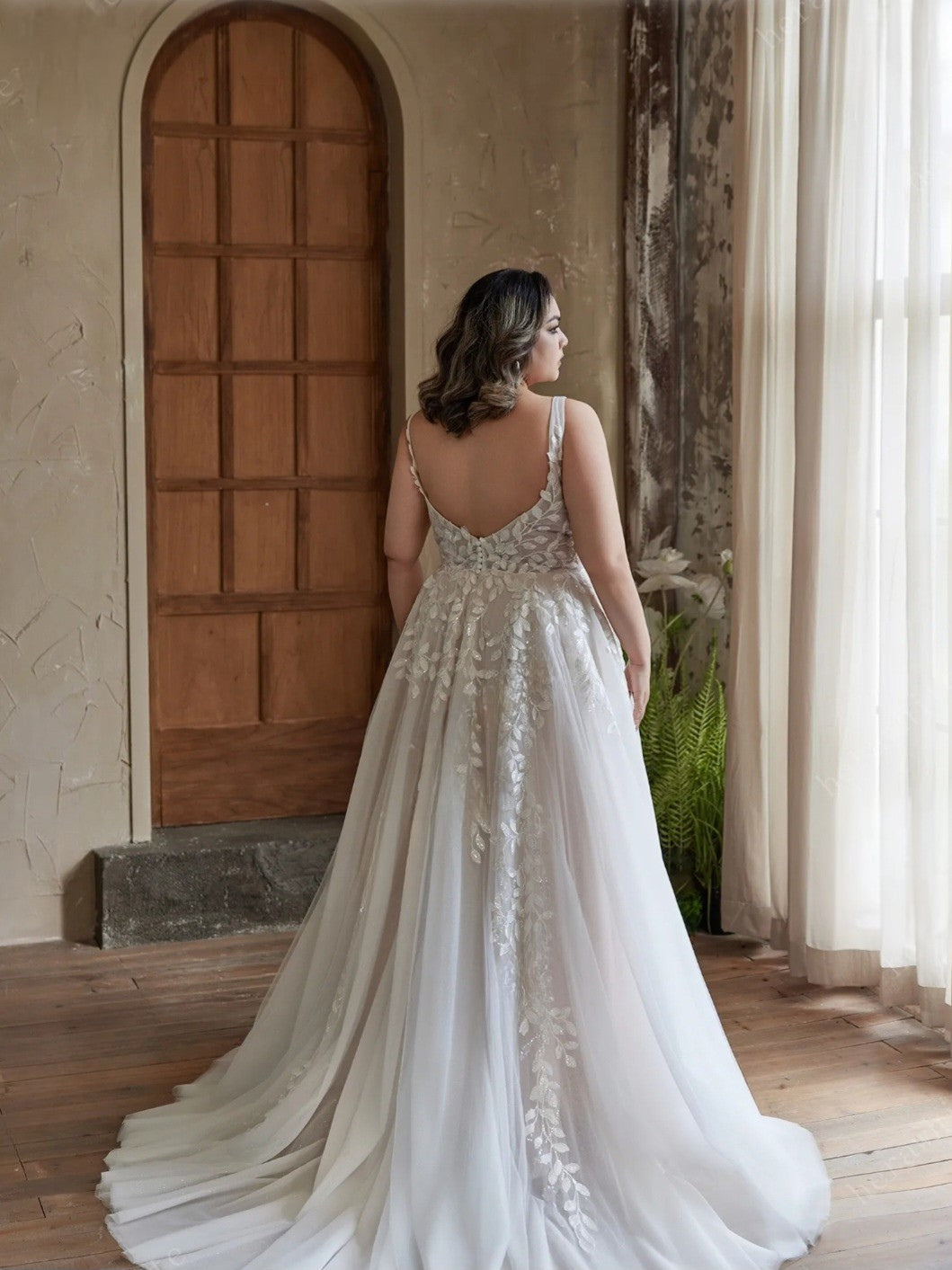 Woman in a white wedding dress standing in a room with wooden door and large window.