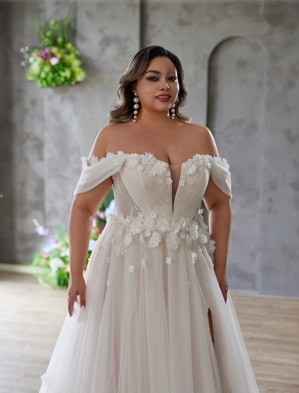 Woman wearing a white wedding dress with floral details in an indoor setting.