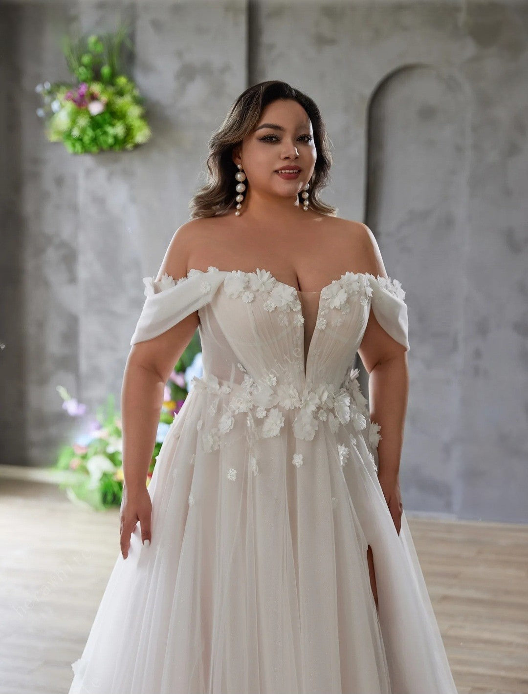 Woman wearing a white wedding dress with floral details in an indoor setting.