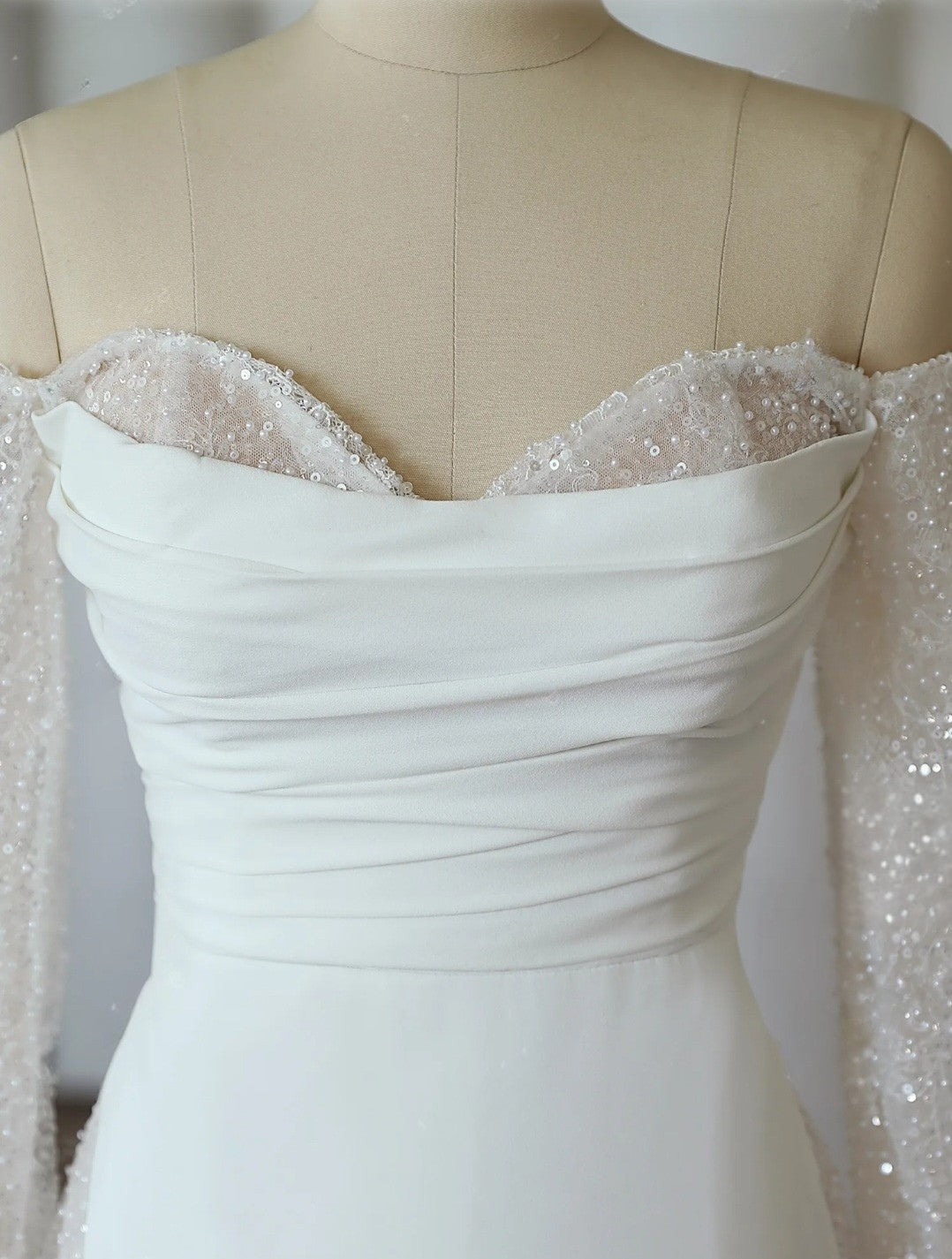 White wedding dress with lace detailing on a mannequin against a neutral background