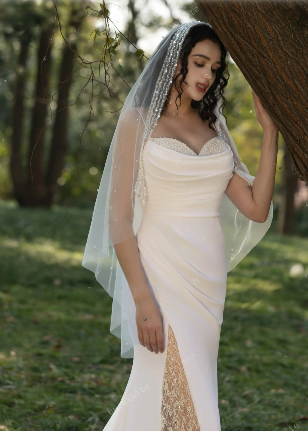 Woman in a white wedding dress with a veil standing outdoors.
