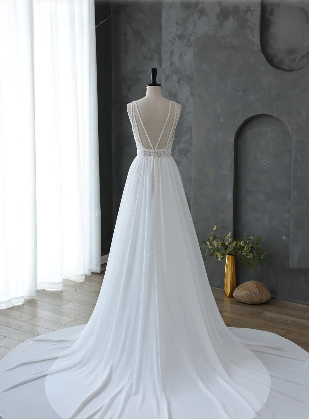White wedding dress on a mannequin against a gray wall with a plant and vase.