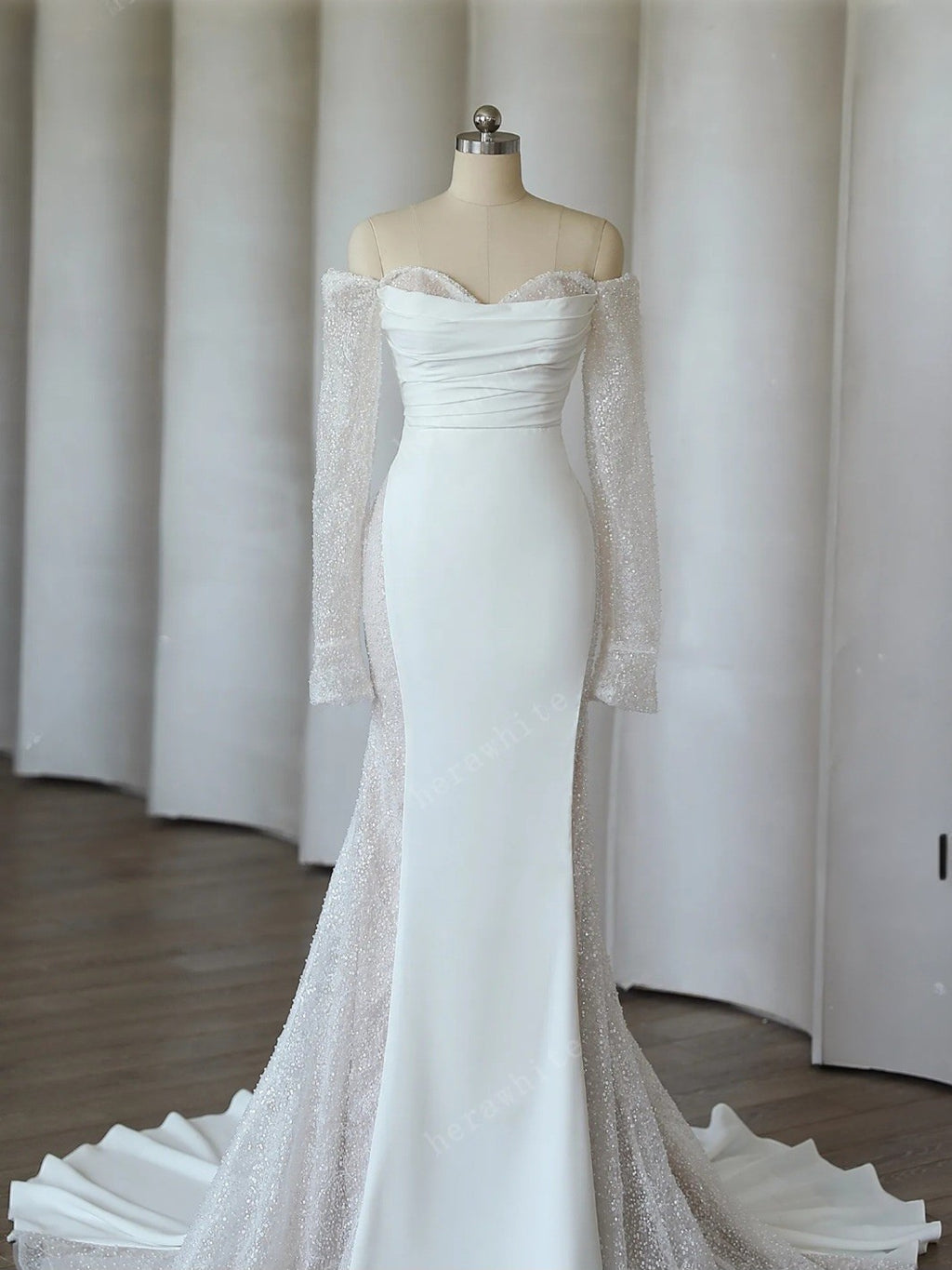 White off-shoulder gown with sheer sleeves on a mannequin against a neutral background