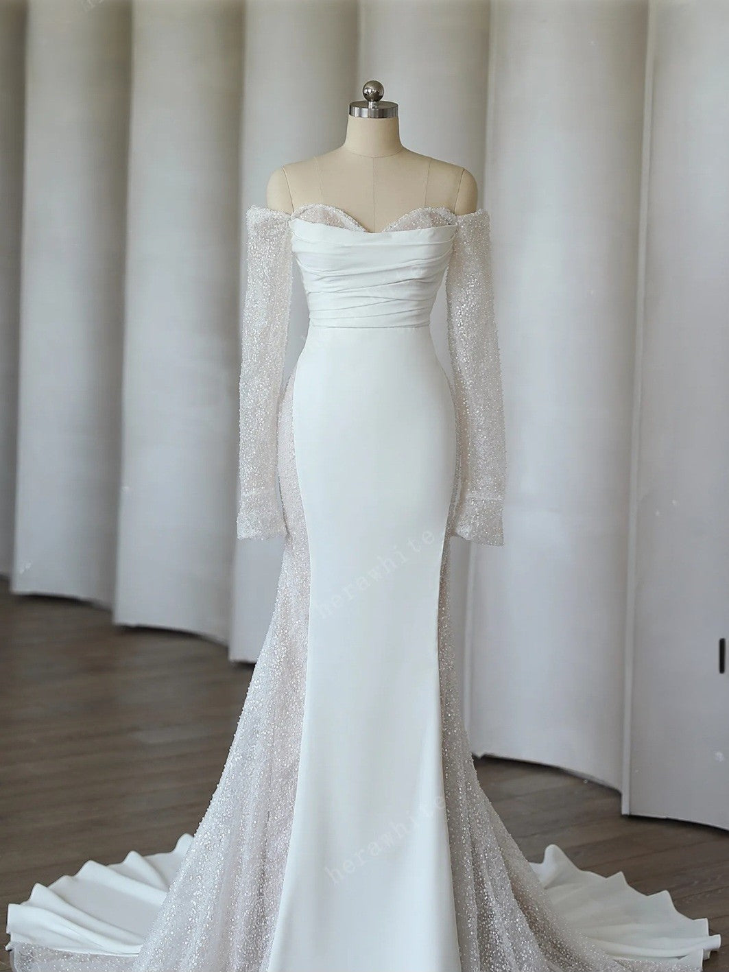 White off-shoulder gown with sheer sleeves on a mannequin against a neutral background