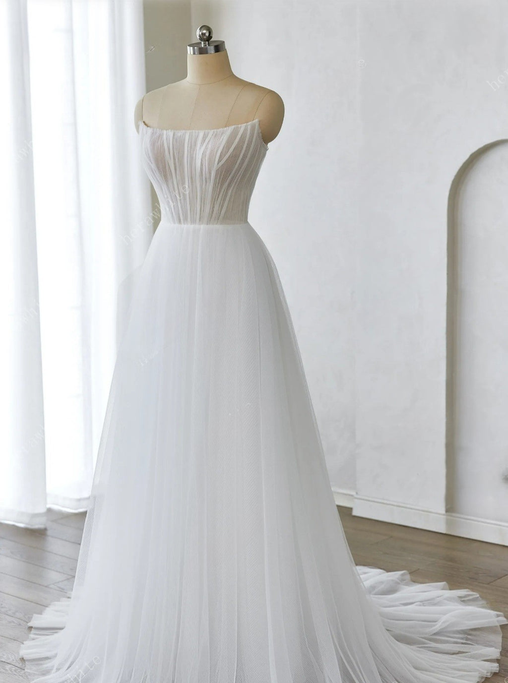 White strapless gown on a mannequin against a white wall.