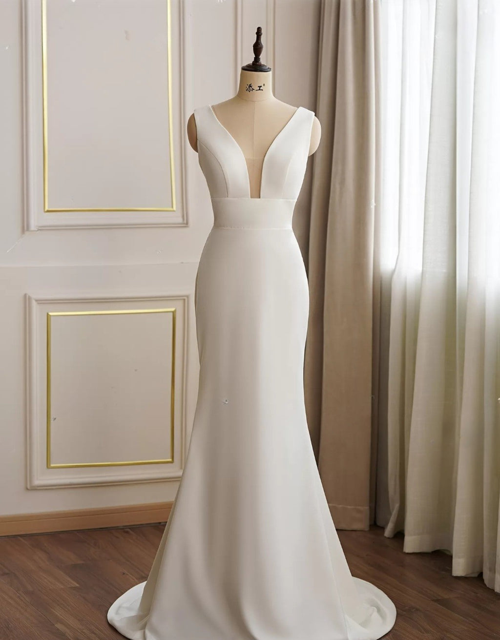 White wedding dress on a mannequin against a neutral wall with curtains.