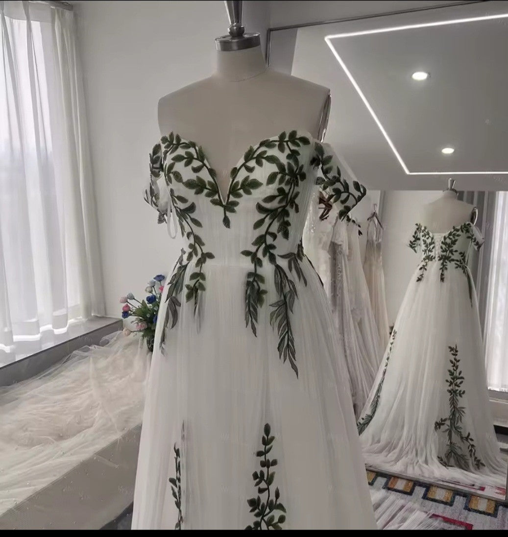 White dress with green leaf patterns on a mannequin in a room with white curtains.