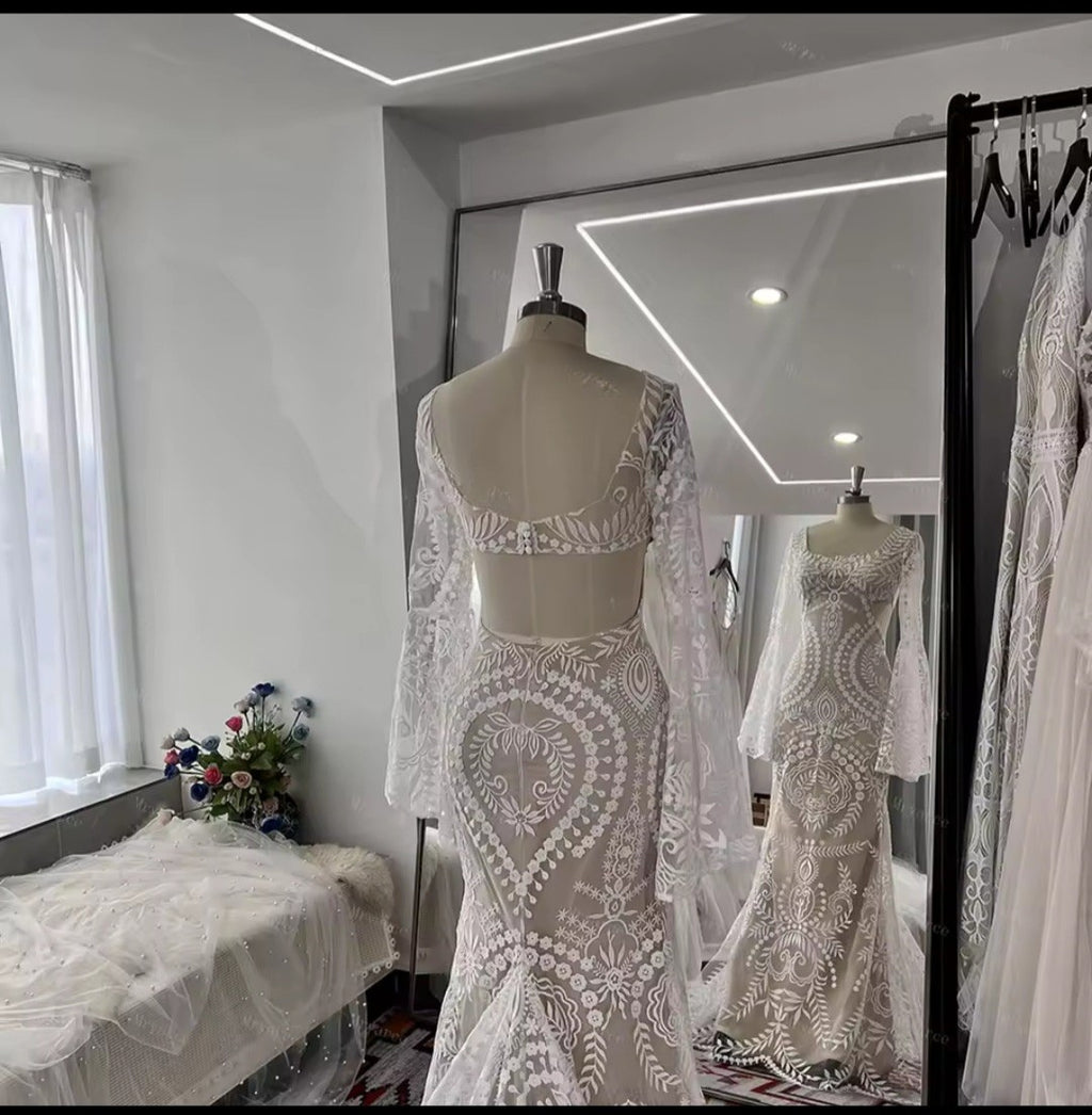 White lace wedding dress on a mannequin in a room with a mirror reflecting the dress.