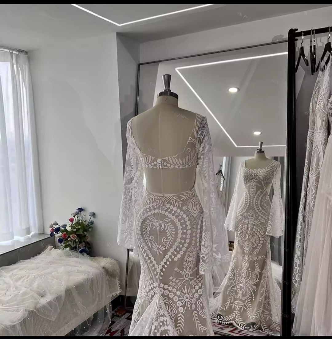 White lace wedding dress on a mannequin in a room with a mirror reflecting the dress.