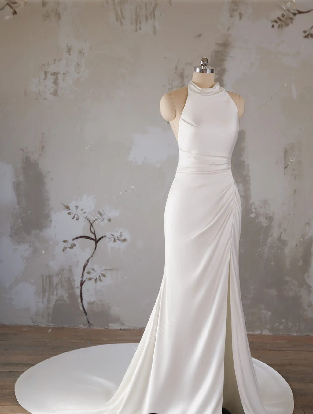 White evening gown on a mannequin against a textured wall.