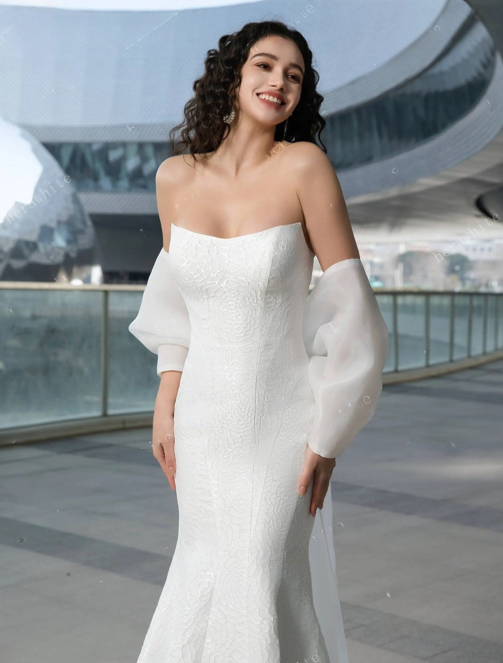 Woman in a white off-shoulder dress standing in front of modern architectural background