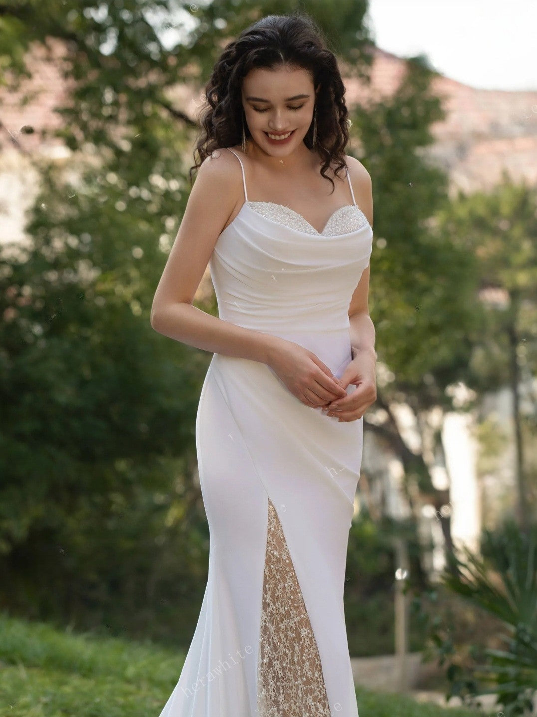 Woman in a white wedding dress with a gold slit standing outdoors.